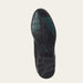 The outsole of a black leather shoe, showing textured tread patterns and green grip accents, photographed from a top-down view on a light beige background.