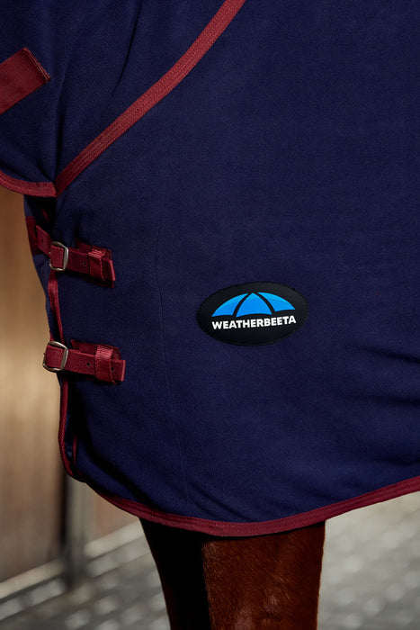 Close-up of the side of the navy blue cooler and hood with dark red trim and straps, featuring a circular Weatherbeeta logo patch on the side.
