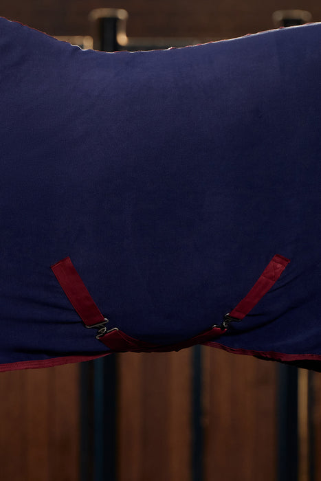 A close-up of a dark navy blue fabric cooler, featuring burgundy surcingles and trim, hanging against a dark wooden background.