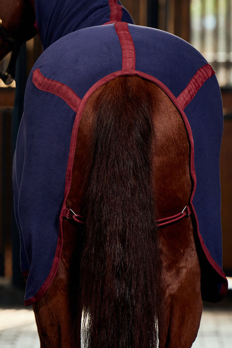 The back of a horse wearing a navy cooler trimmed in burgundy Features the burgundy leg straps wrapped around the back legs and up to the cooler. 