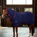 A brown horse standing in a stable wearing a navy blue cooler with burgundy trim and straps and detachable hood. The stable has wooden stalls and large windows in the background.