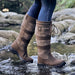 Brown knee-high boots with striped design and ties at the top for cinching at the calf worn by a woman walking through shallow water.