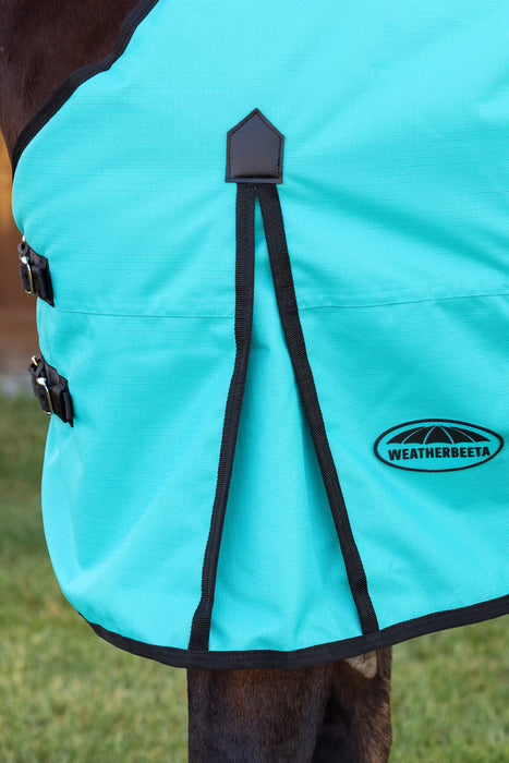 A close-up of a turquoise horse blanket shoulder gusset with black trim and straps, featuring the WeatherBeeta logo on the lower right, shown on a horse outdoors.