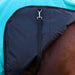 Close-up of a horse blanket draped over a horse's body, showing a turquoise blue upper section, a black neck panel with a black strap and silver buckle, and the horse's brown coat underneath, against a wooden fence background.