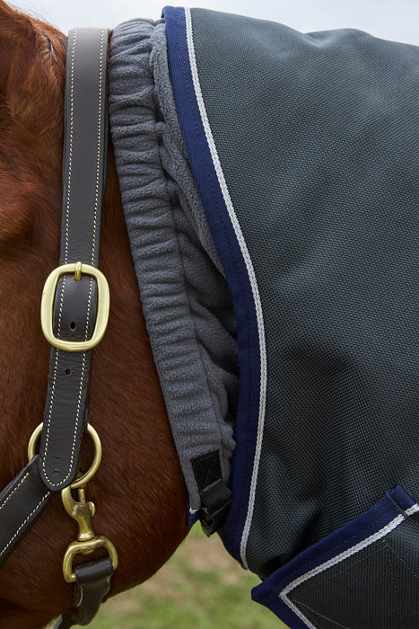 Close-up of a horse wearing a dark gray turnout blanket with navy blue and white trim, along with a dark gray leather halter with brass hardware.