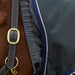 Close-up of a horse wearing a dark gray turnout blanket with navy blue and white trim, along with a dark gray leather halter with brass hardware.