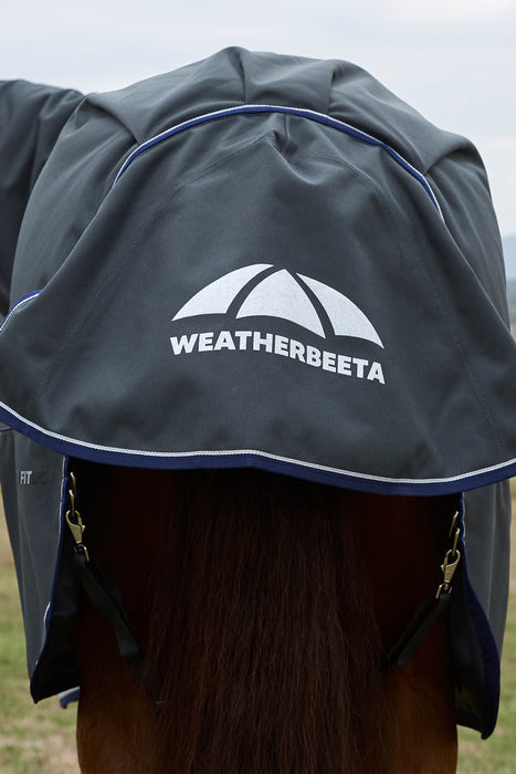 A close-up of a horse turnout blanket with an attached neck cover, shown on a horse from behind. The cover is dark gray with a white Weatherbeeta logo and white piping, with blue trim along the edge.