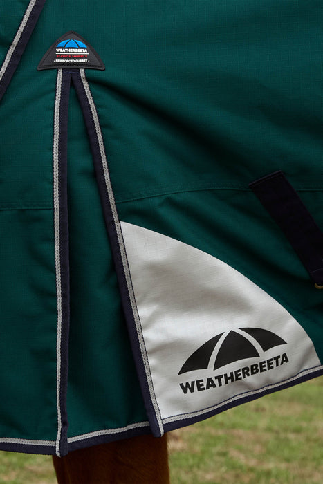 Close-up of a dark green Weatherbeeta horse blanket with navy and white piping, a white diagonal panel with the black Weatherbeeta logo, and a small Weatherbeeta brand patch near the top.