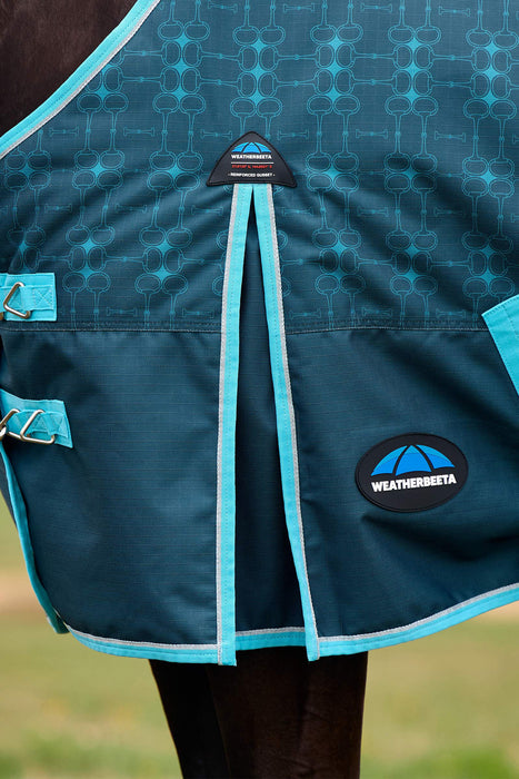 Close-up of a horse blanket with a dark teal patterned upper section, bright turquoise piping, and a Weatherbeta logo patch on the lower right.