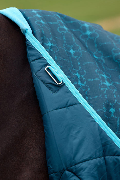 Close-up of a quilted equestrian saddle pad in teal blue with a subtle geometric pattern, featuring a silver metal D-ring attachment and a bright turquoise trim, shown on a horse.