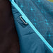 Close-up of a quilted equestrian saddle pad in teal blue with a subtle geometric pattern, featuring a silver metal D-ring attachment and a bright turquoise trim, shown on a horse.