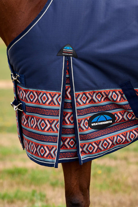 Close-up of a horse blanket on a horse, showing navy blue fabric with a red, white, and blue geometric patterned lower section and a visible WeatherBeta logo patch.