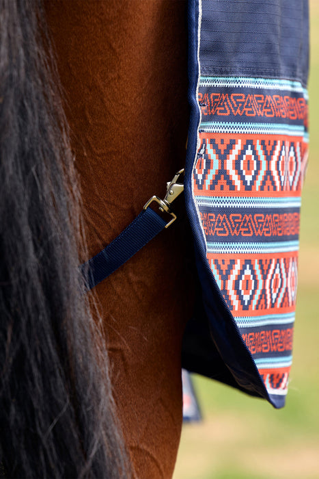 Close-up of a horse's brown coat and dark tail with a navy blue patterned turnout blanket draped over the rump, featuring geometric orange, white, and blue woven-style motifs.