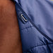 Close-up of a navy blue quilted horse blanket or tack garment with a silver metal D-ring attachment, shown on a brown horse against an outdoor blurred background.
