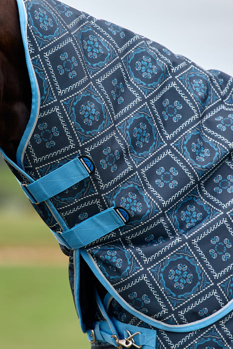 Close-up of a horse turnout blanket with a navy blue and teal geometric pattern, featuring blue straps and trim.