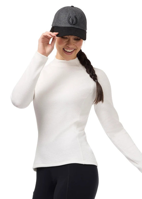 A woman wearing a fitted white mock-neck long-sleeve top, black leggings, and a dark gray baseball cap with a circular Kerrits logo, posing against a solid white background.
