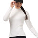 A woman wearing a fitted white mock-neck long-sleeve top, black leggings, and a dark gray baseball cap with a circular Kerrits logo, posing against a solid white background.