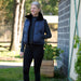 A woman standing in equestrian clothing outside of a brick barn in the front drive 