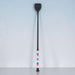 A long black riding crop or equestrian staff with a colorful striped grip section, standing upright against a light gray textured wall.