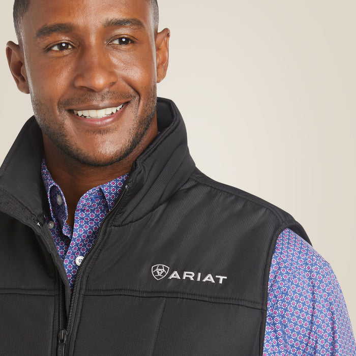 A smiling man wearing a black Ariat zip-front vest over a blue and red patterned button-down shirt, photographed against a plain light beige background.