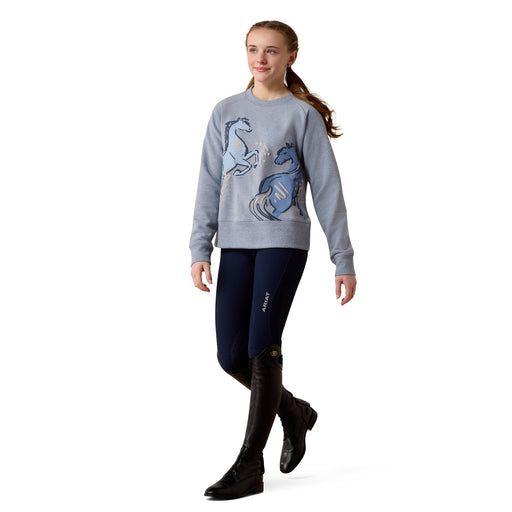 A Young Person wearing a gray sweater with horse designs and navy riding pants on a white background