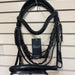 Black leather and braided equestrian bridle hanging on a wall display hook, with a black hangtag attached. The bridle includes a browband, bit area, cheekpieces, and reins, shown against a white slatwall background.
