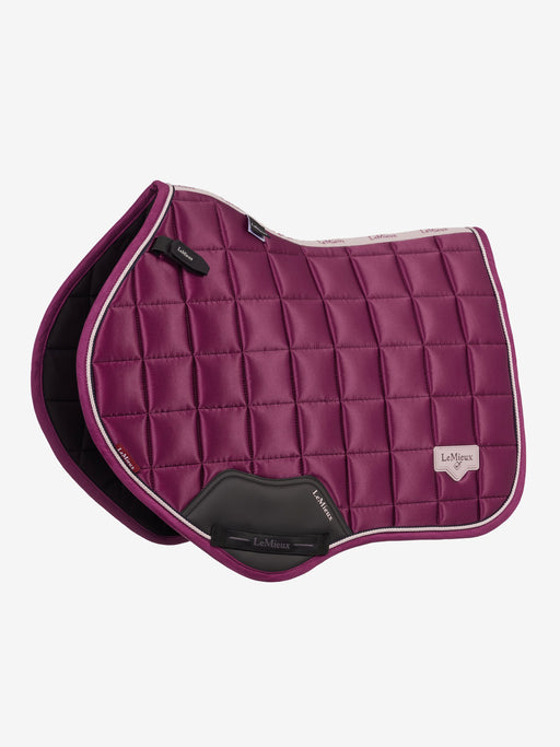 A quilted equestrian saddle pad in deep magenta-purple with white piping and a black leather LeMieux brand pad flap, shown on a light gray background.
