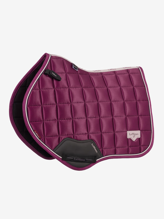 A quilted equestrian saddle pad in deep magenta-purple with white piping and a black leather LeMieux brand pad flap, shown on a light gray background.