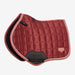 A quilted equestrian saddle pad in a dusty rose orange color, featuring a diamond-quilted pattern, a black protective under-rib pad, and a light coral stitched border, shown against a plain light gray background.