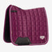 A LeMieux quilted horse saddle pad in a deep magenta-purple color, featuring a diamond-quilted pattern, white piping, and black leather accents, shown against a light gray background.
