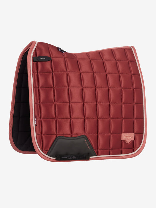 A quilted equestrian saddle pad in a deep brick red color, featuring a diamond-quilted pattern, a black leather gullet panel, and a light pink piping border, shown against a plain light gray background.