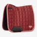 A quilted equestrian saddle pad in a deep brick red color, featuring a diamond-quilted pattern, a black leather gullet panel, and a light pink piping border, shown against a plain light gray background.