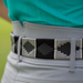 A close-up of a person wearing a light gray belt with black geometric pixelated patterns, paired with a turquoise top and light gray pants.