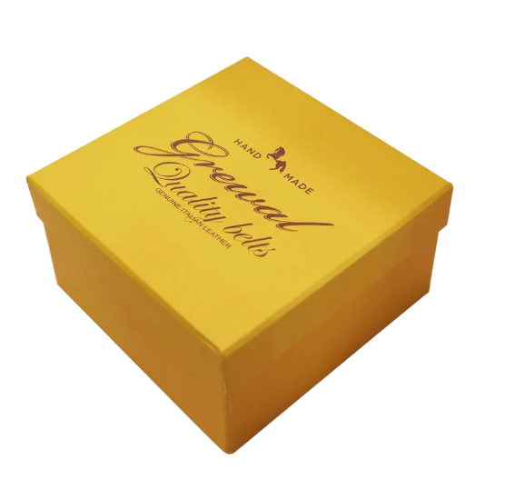A square yellow gift box with a hinged lid, featuring the text 'Elegant Quality belts HAND MADE' printed in brown on the lid, set against a plain white background.