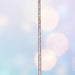A unicorn-themed riding crop with a sparkly unicorn head at the top, a long sparkly shaft, and a dark textured handle, shown against a soft pastel bokeh background.