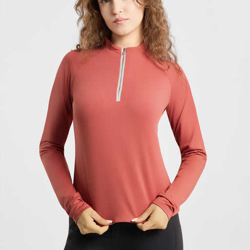 A woman wearing a long-sleeve athletic quarter-zip top in a muted terracotta or dusty rose color, paired with black bottoms, against a clean light gray studio background.
