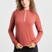 A woman wearing a long-sleeve athletic quarter-zip top in a muted terracotta or dusty rose color, paired with black bottoms, against a clean light gray studio background.