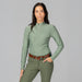 A women wearing a long-sleeve athletic quarter-zip top in a muted sage green color, featuring perforated side panels and a high mock neck collar, displayed on a mannequin torso against a plain grey background.