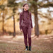 Girl in maroon equestrian outfit standing in a forest during autumn.