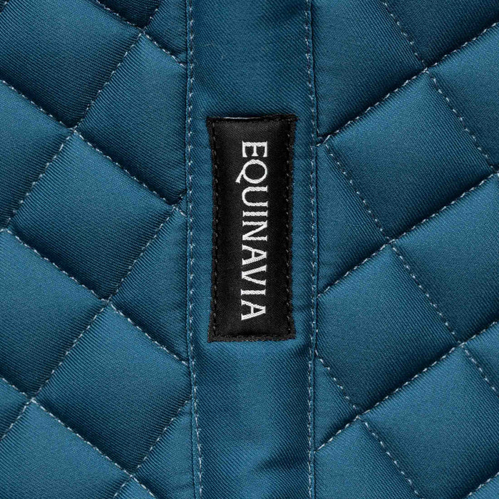 Close-up of a blue quilted fabric saddle pad with 'Equinavia' label on the spine